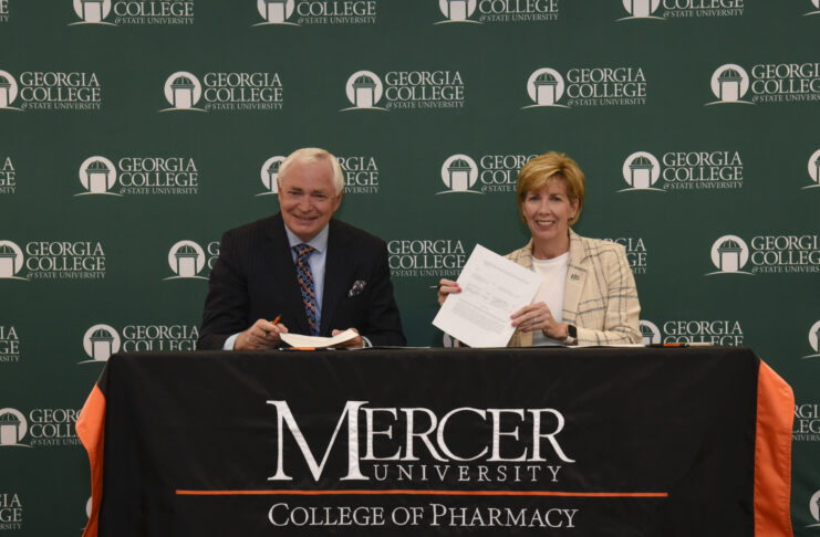 GCSU president holds up a piece of paper. Mercer president sits on her left.