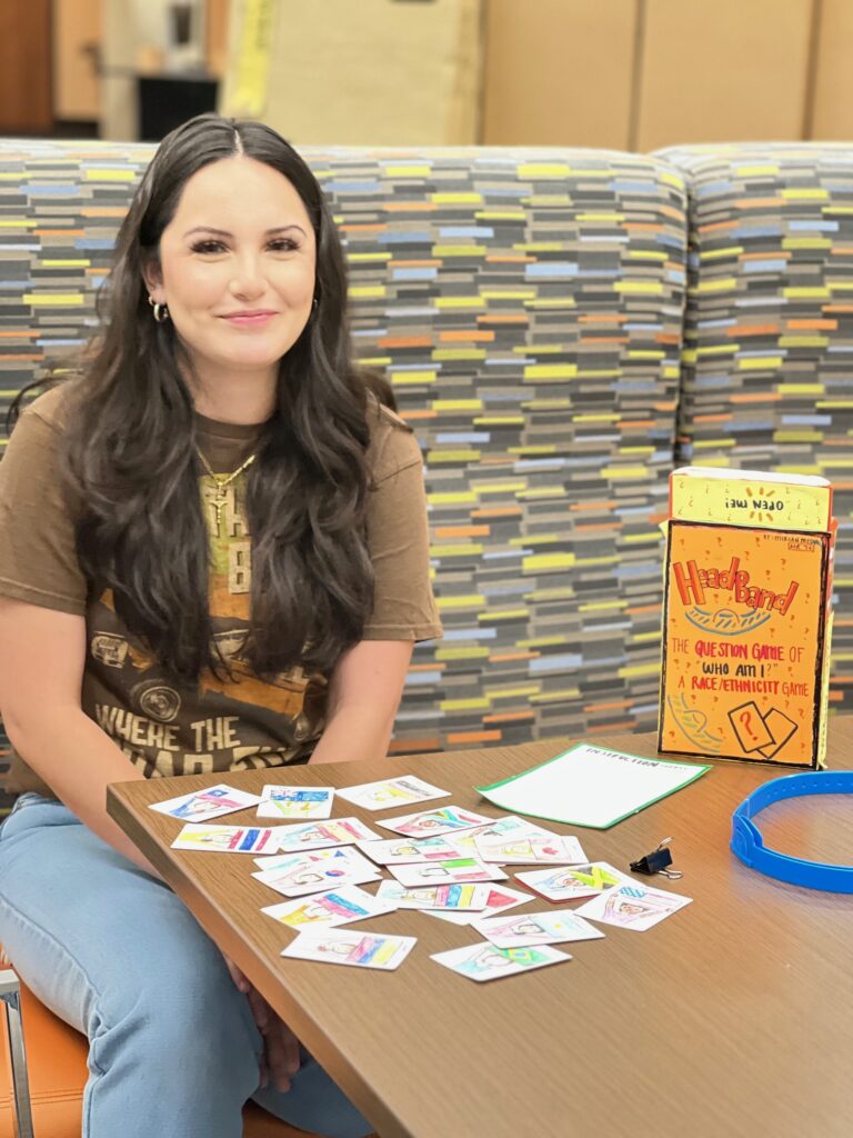 A student sits at a booth with a pile of game cards on a table in front of her.