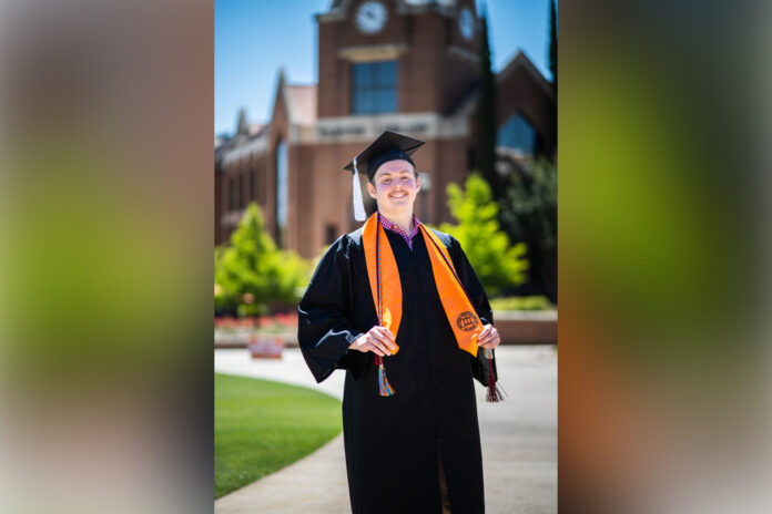 Sam Tupper wears graduation cap and gown, standing in front of the library