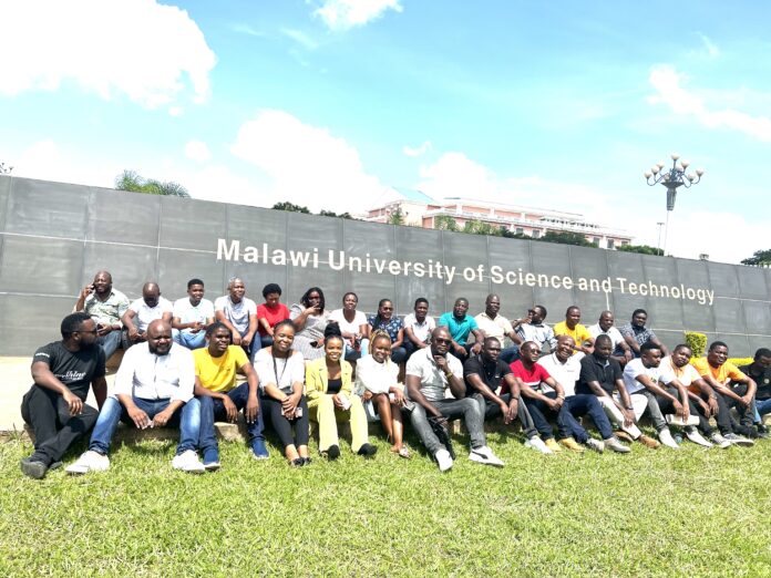 A group of people is shown in front of a sign for Malawi University of Science and Technology.