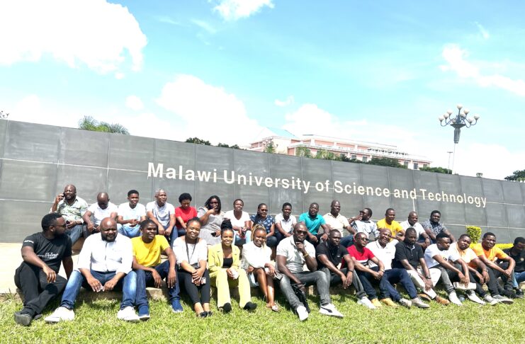 A group of people is shown in front of a sign for Malawi University of Science and Technology.