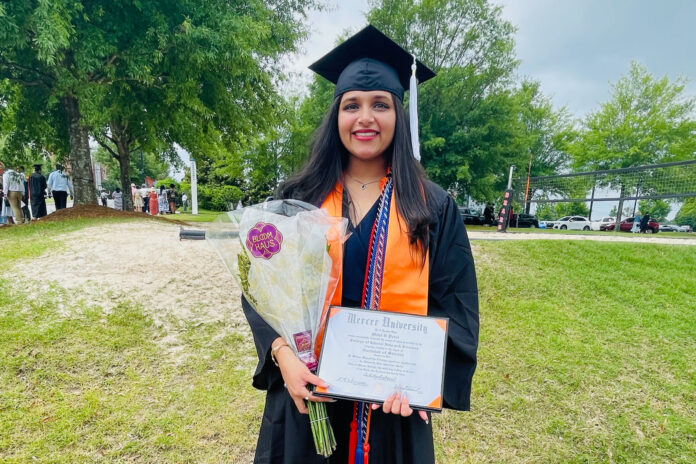 Mahi Patel, wearing graduation cap and gown, holds flowers and her diploma