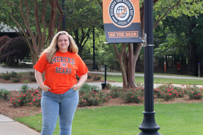 samantha cannon stands next to a banner on mercer's campus.