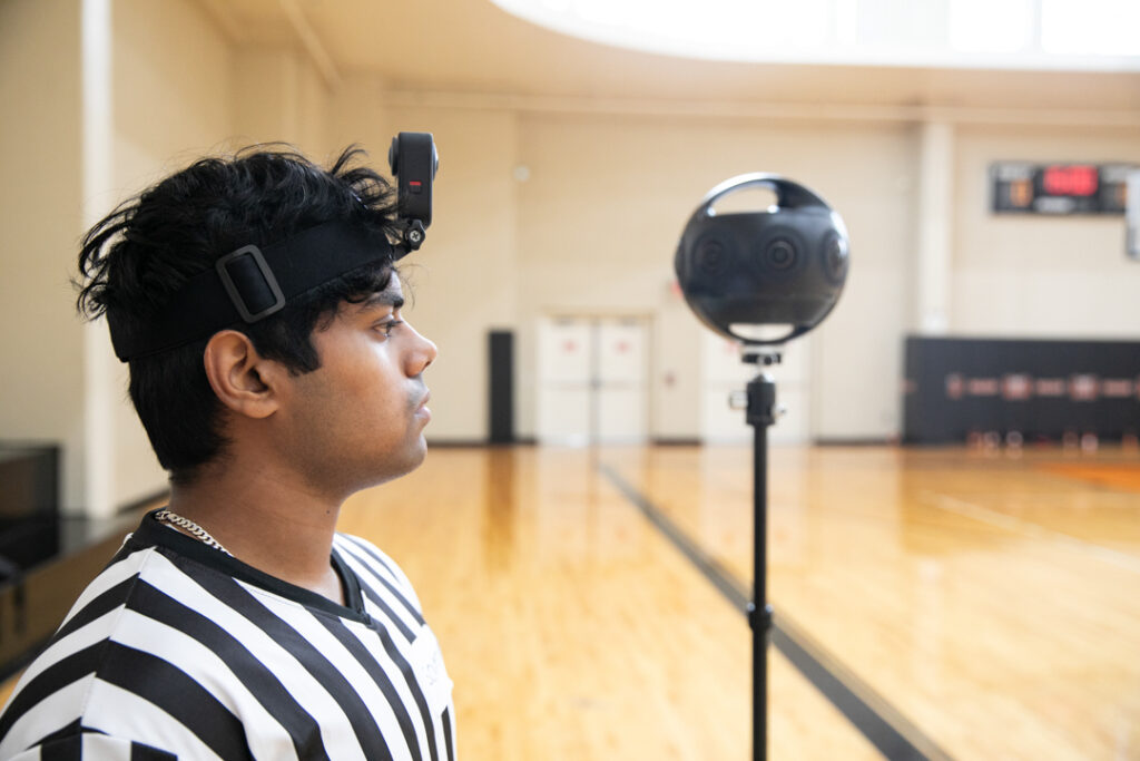 A mercer student wears a go pro on his head. a 360 camera is in the background.