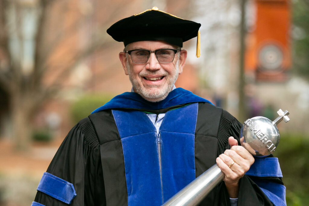 man in faculty graduation regalia holding a mace