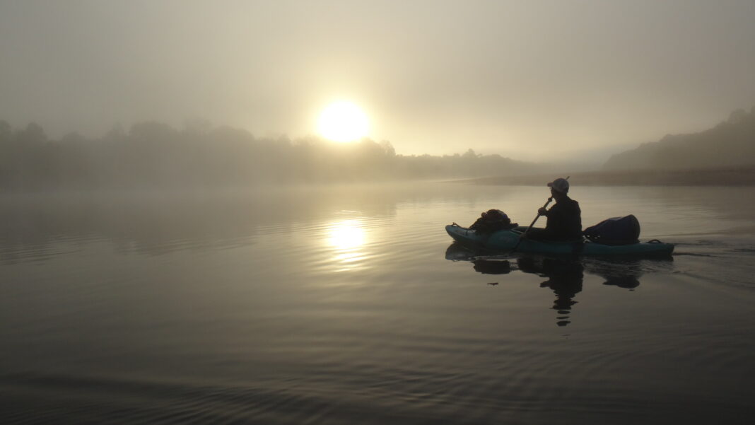 A man in a kayak are shown on a river.