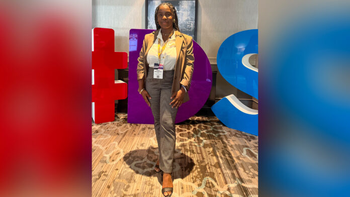 A woman in business wear stands in front of a sign for the Black Enterprise Disruptor Summit.