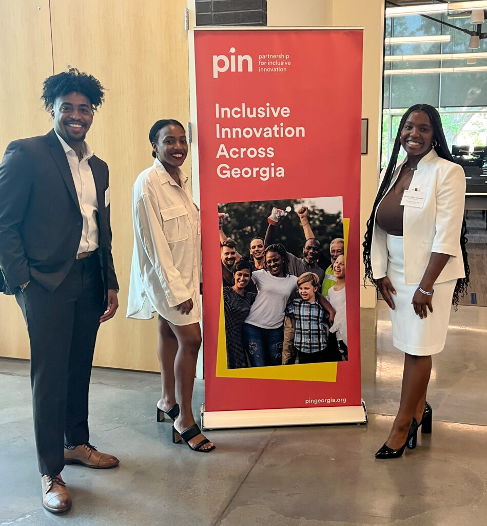 Three people stand in front of a banner for the Partnership for Inclusive Innovation.