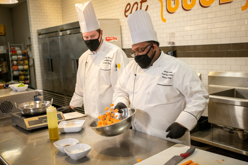 Two chefs wear their uniforms and cook in the kitchen.