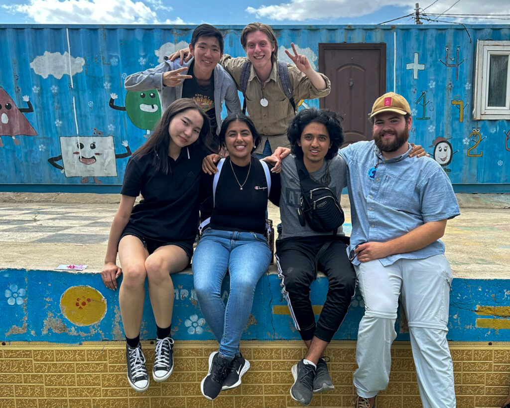 Six people pose in front of a bright blue building.
