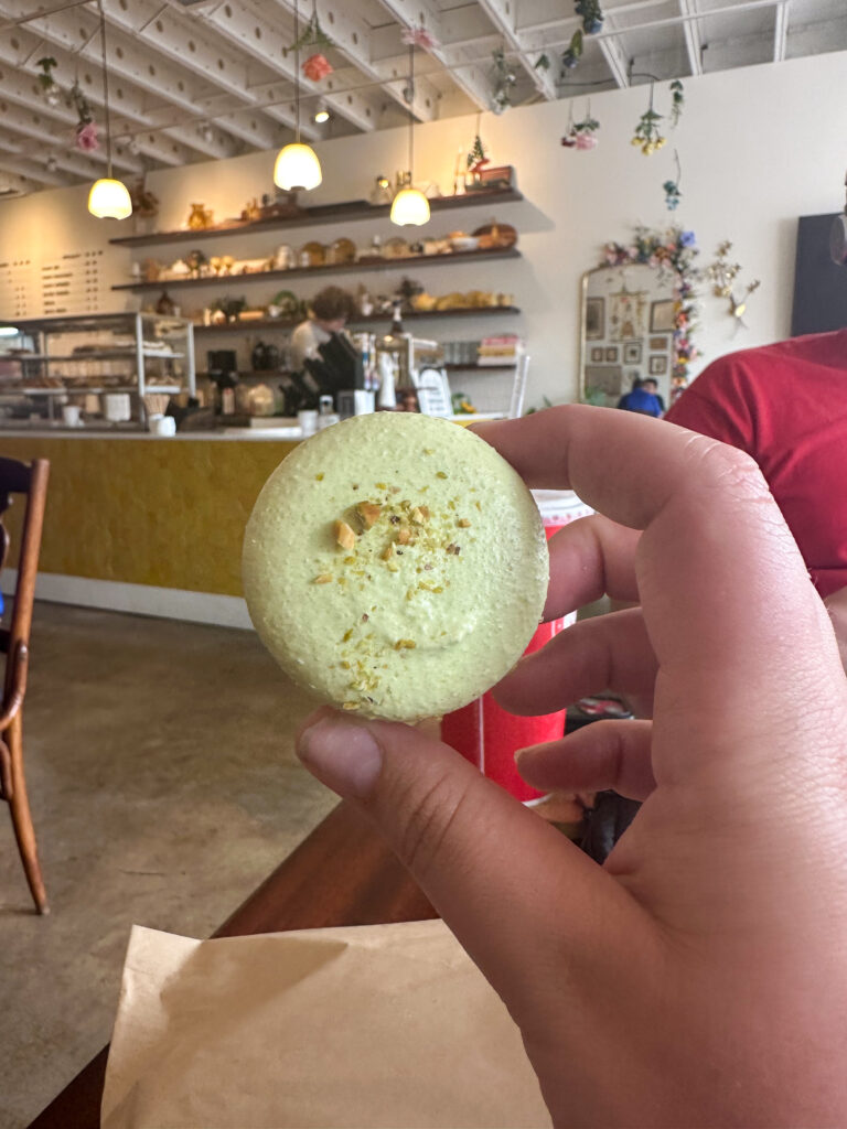A hand holds up a yellow macaroon inside a store.