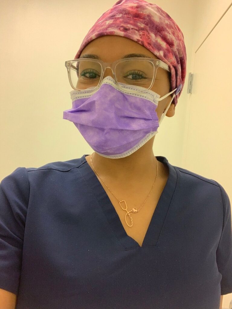 A woman is shown in scrubs, a scrub cap and mask.