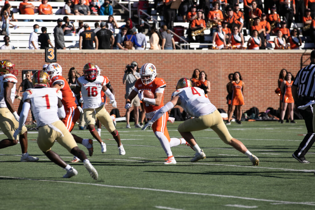 a mercer player in an orange jersey runs with a football while vmi players in white jerseys try to tackle him