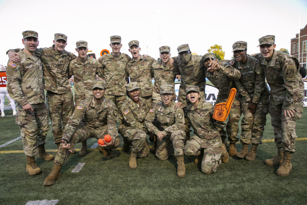 People in fatigues cheer and hold a foam finger for the Mercer Bears