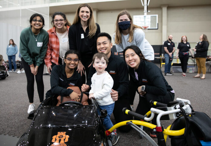 group of smiling college students surrounding young child and a toy car