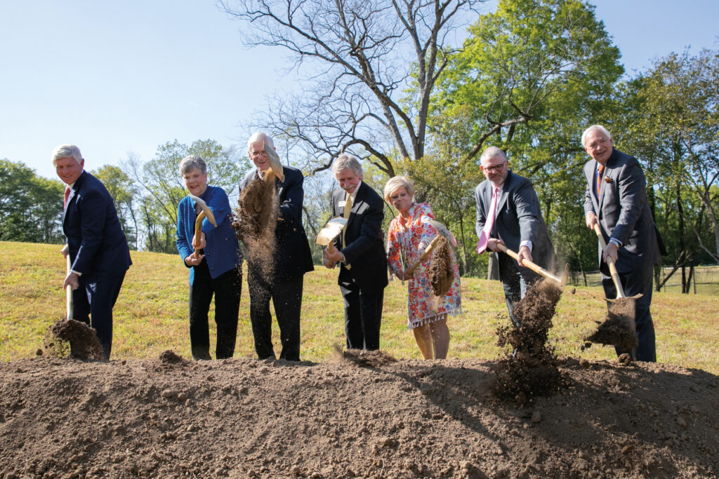 seven people hold shovels and ceremoniously toss from a pile of dirt