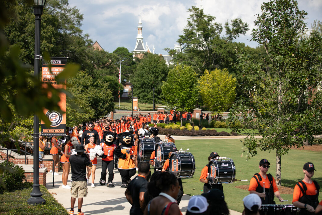 percussionists, toby and tot mascots, cheerleaders and football players process down a sidewalk