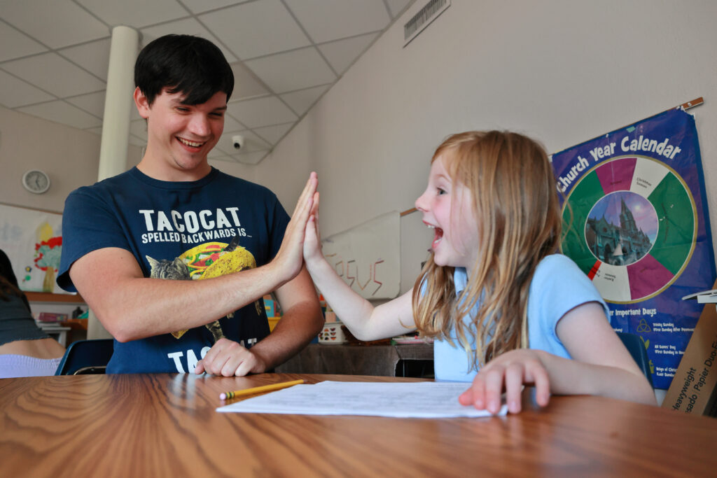 A college student gives a child a high five while they sit at a table.
