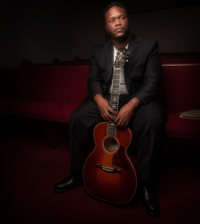 Blues musician Jontavious Willis seated holding guitar