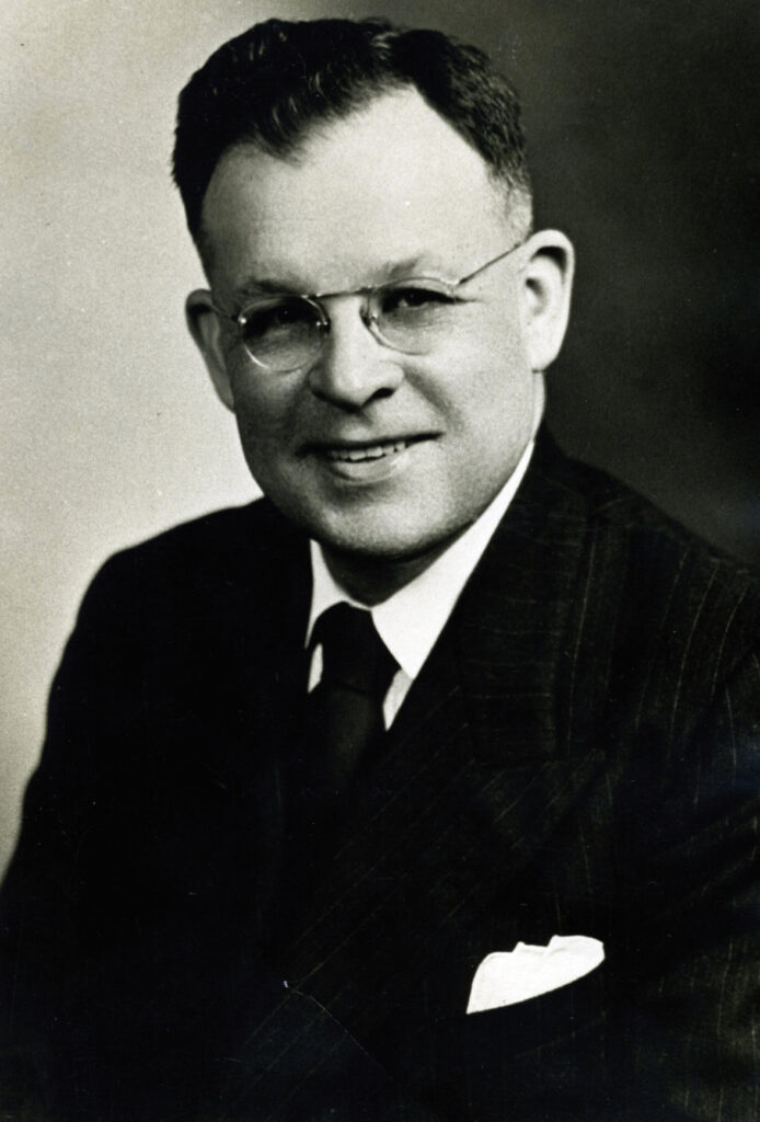 headshot of man in suit, tie and glasses