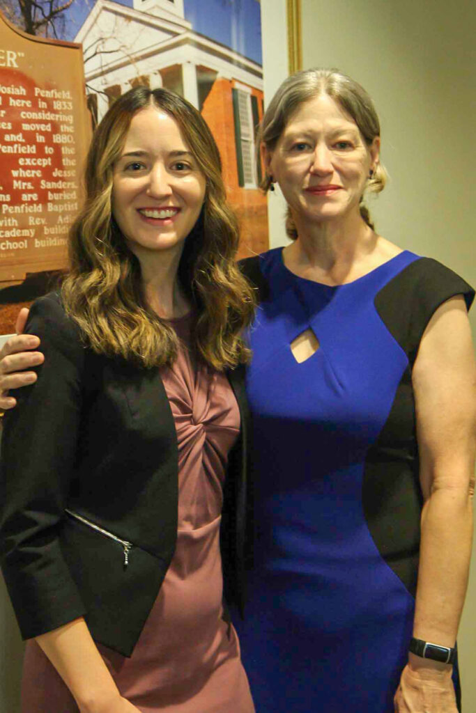 a woman in a blue dress puts her arm around a younger woman in a pink dress and black dress jacket