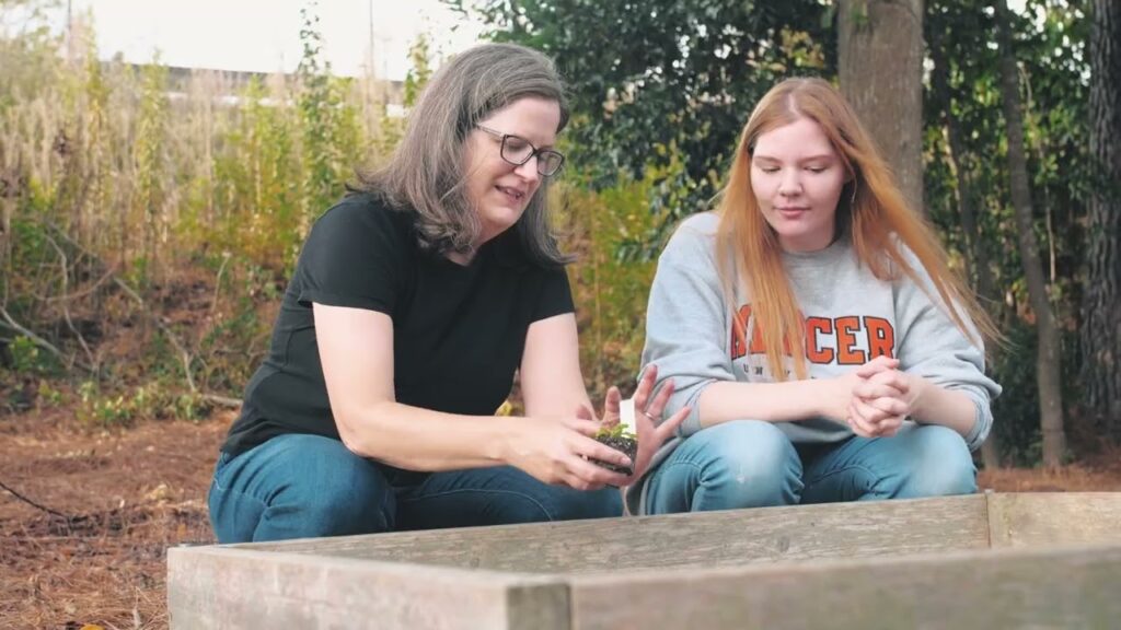 a professor and a student put a small plant in a bed