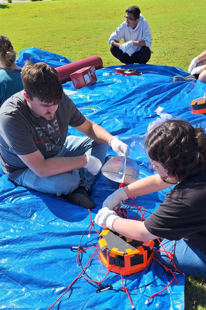 students work on a piece of equipment on a blue tarp