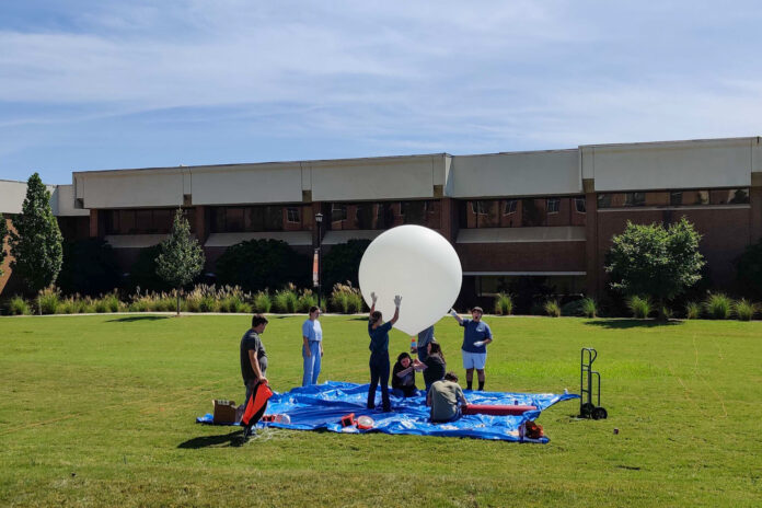 students in a field blow up a big white balloon