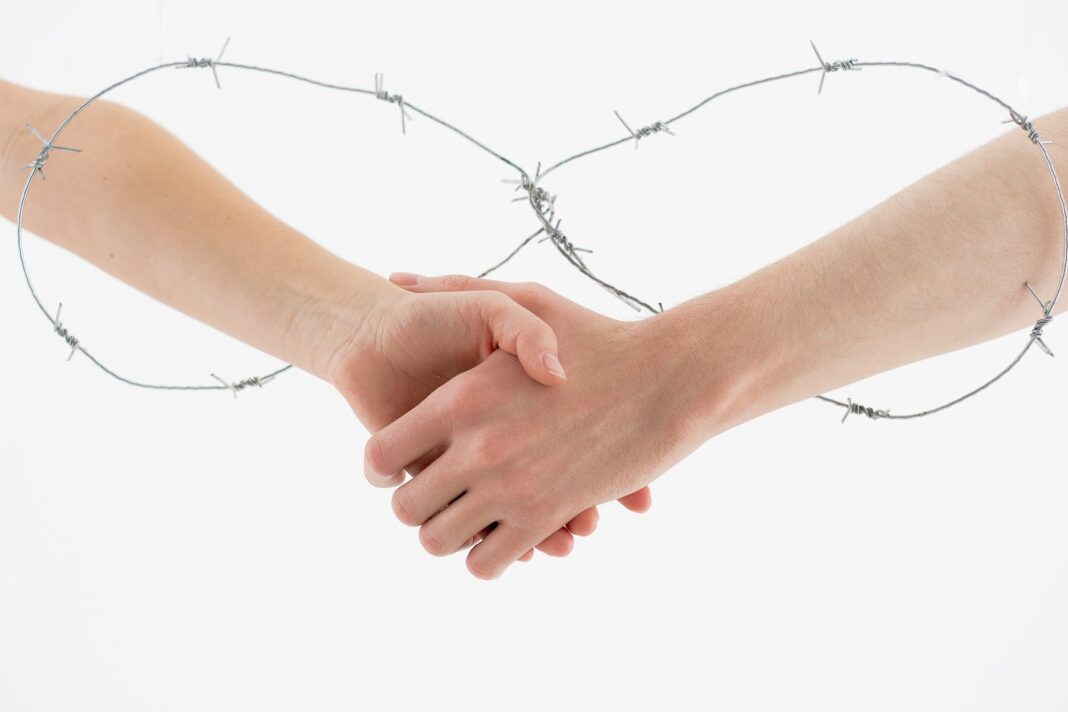 Two People Shaking Hands Through Barbed Wire