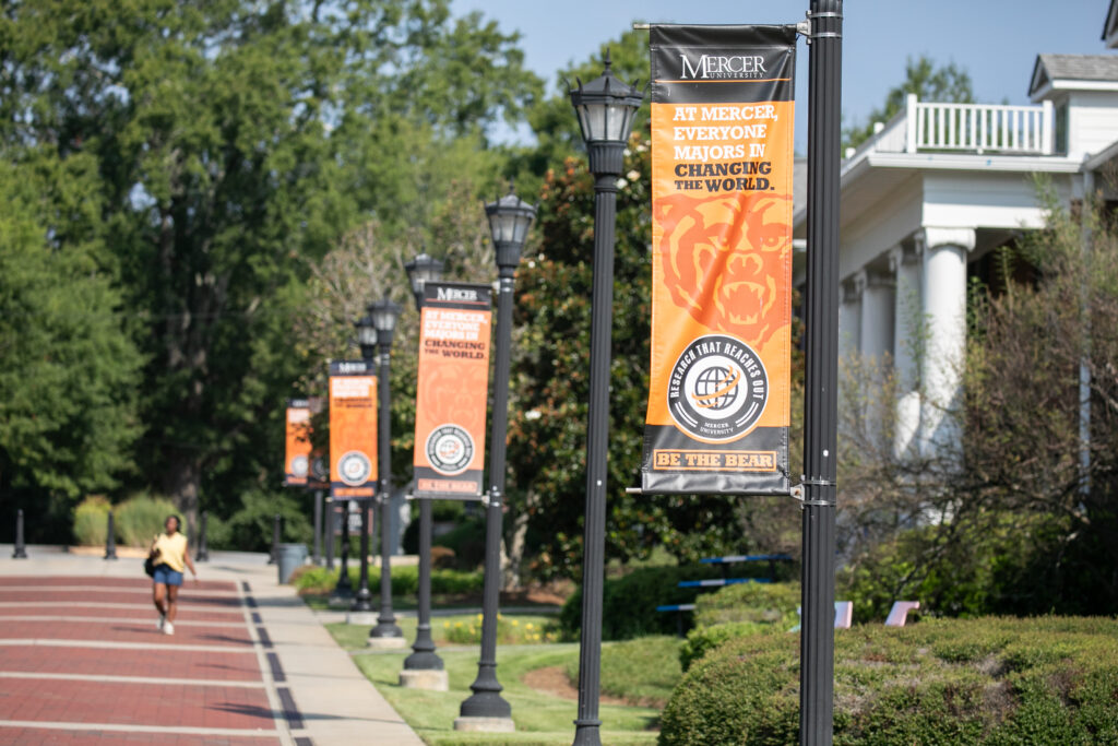 Exterior campus street posts with orangge banners stating "At Mercer Everyone Majors In Changing the World"