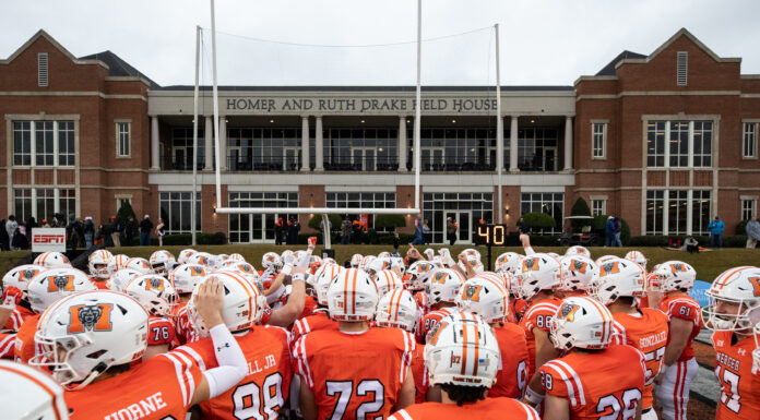 Mercer Football Makes History, Will Host First-Round FCS Playoff Game on Saturday The backs of football players in uniform are seen in front of the goal post and field house.