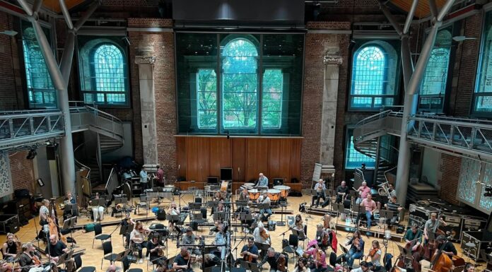 Recording, documentary projects highlight talents of Mercer and Macon musicians Orchestra musicians can be seen at their seats with their instruments, in a large open venue with large windows behind them.