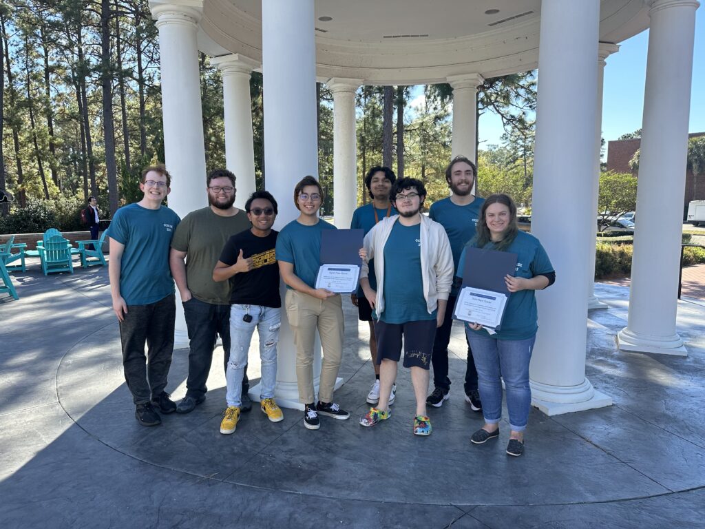 Eight smiling college students standing in front of columns holding award certificates