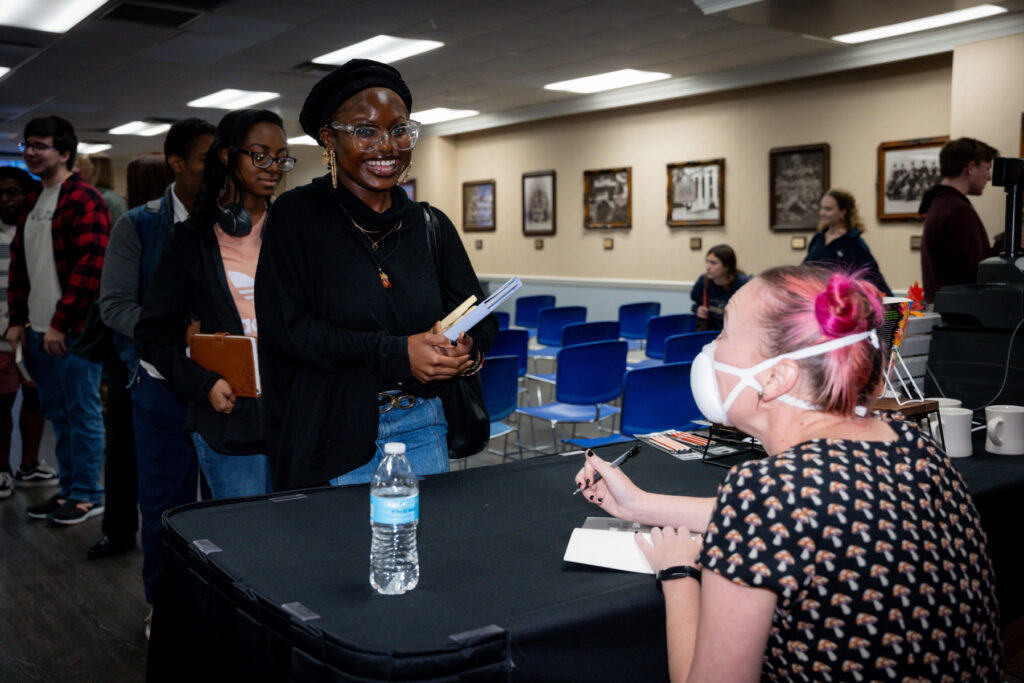 gwen kirby sits at a table signing a book while a young woman looks on