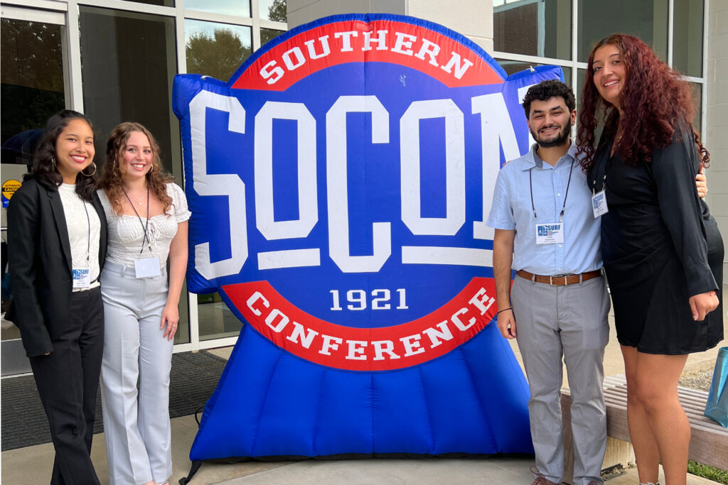 four students said on either side of a blow-up SoCon logo