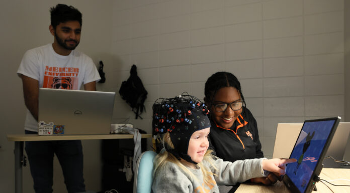 Mercer research aims to identify earlier signs of disorders like ADHD, autism Parth Patel stands at a computer, while Lynzi Holland sits at a table with a child wearing a cap with the fNIRS technology.