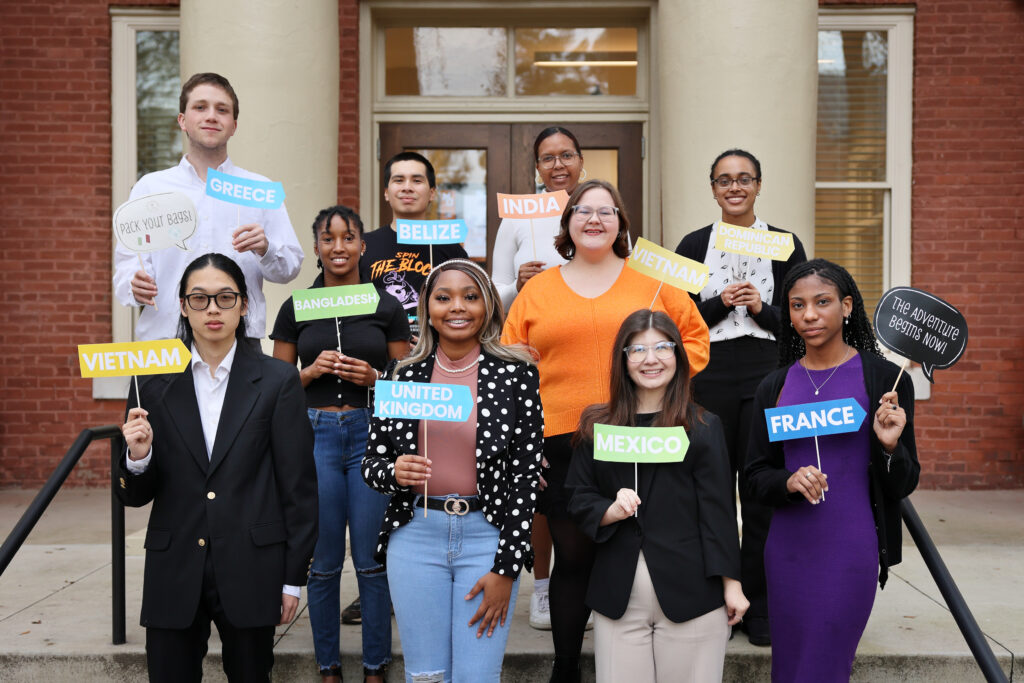 10 male and female college students standing smiling holding signs with country names printed on them