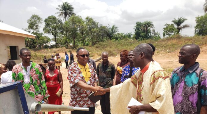 Mercer alumnus dedicated to bringing clean water to Liberians Two men shake hands, while other stand around them in a circle, near a water well.
