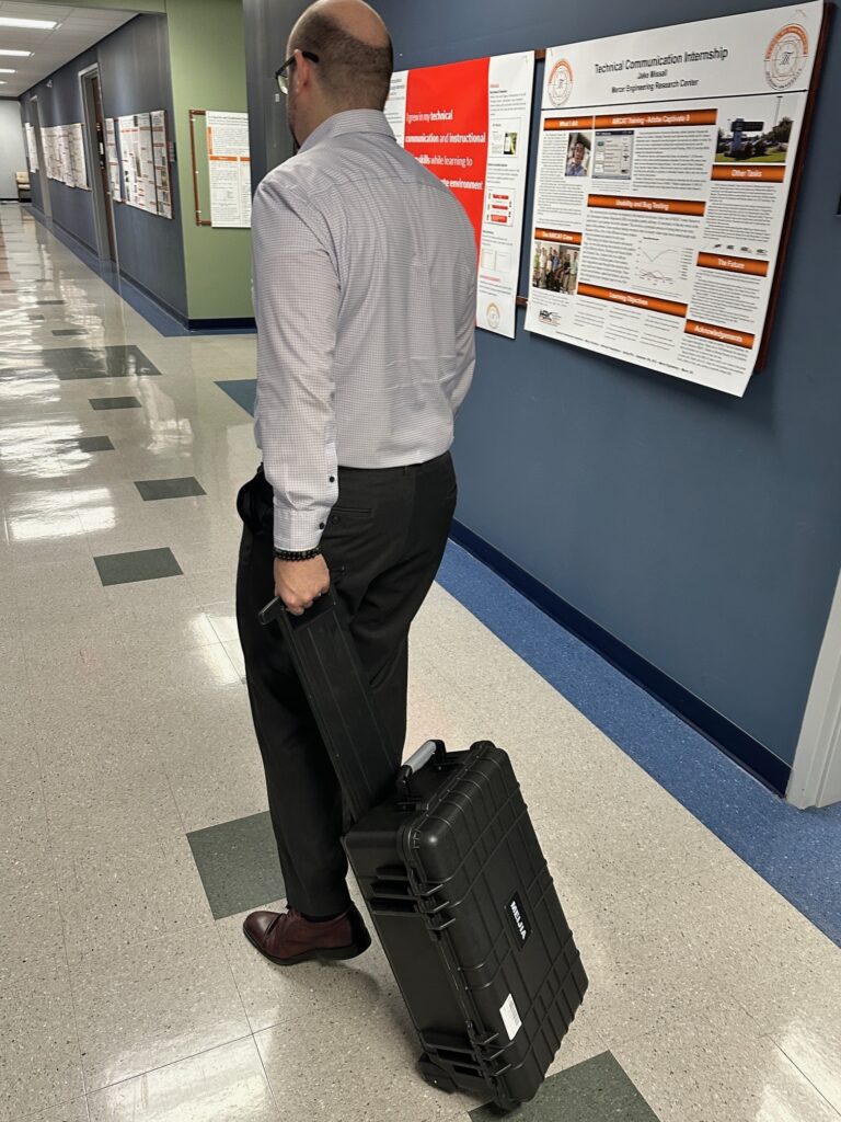 A man rolls a suitcase down a hallway.