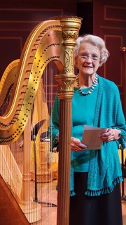 older woman stands next to harp