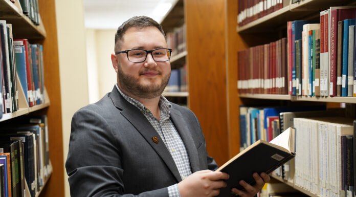 Mercer Law student wants to help others prepare for difficult times A man in a suit stands holding a book in a library