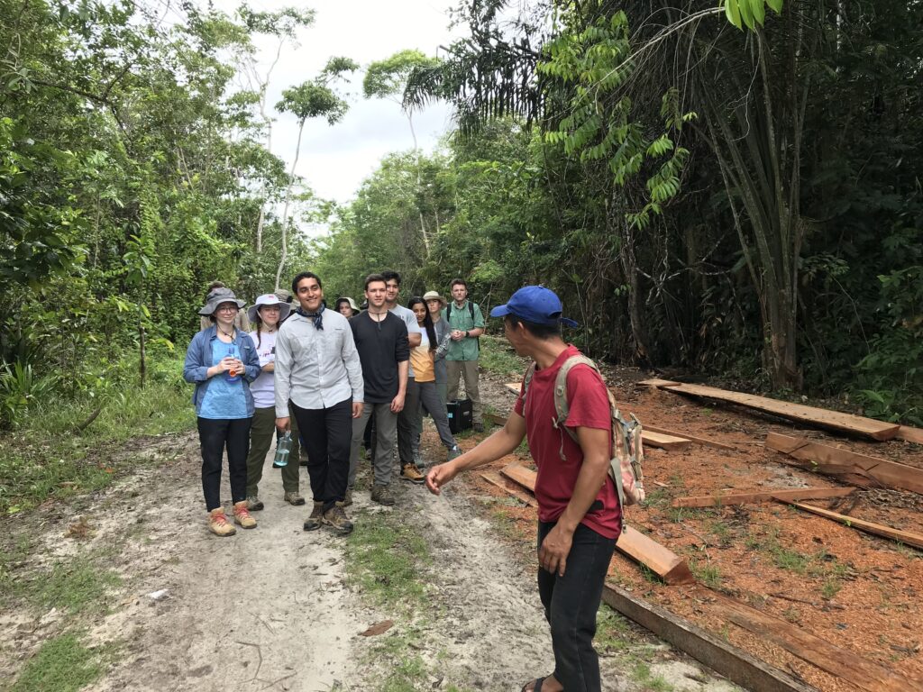 A group of students talks with a man as they walk down a dirt path.
