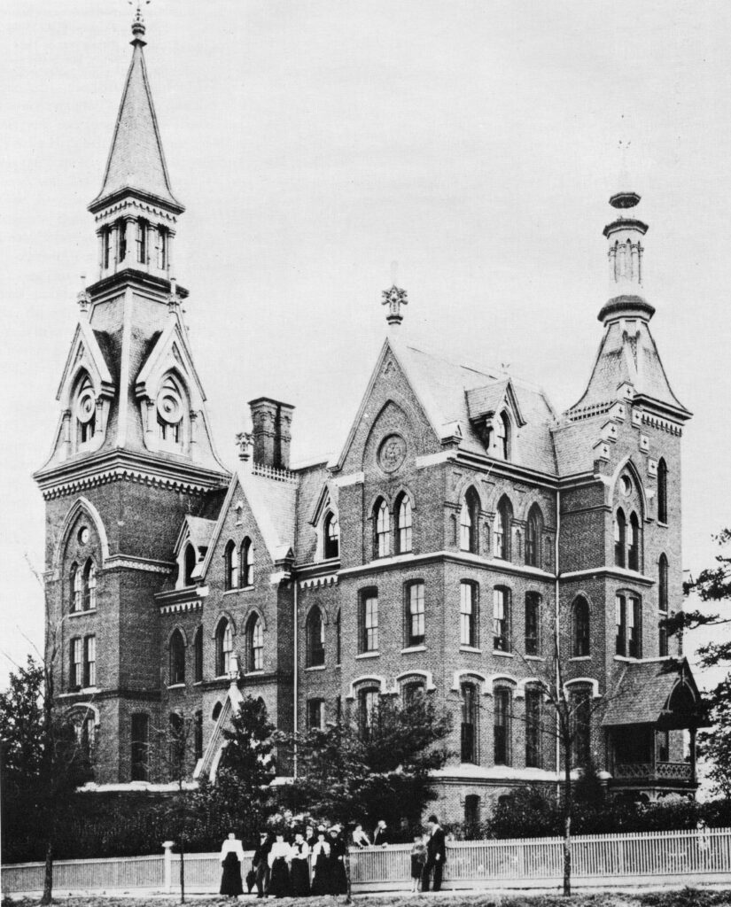 A black and white photo of a five-story brick building with three towers.