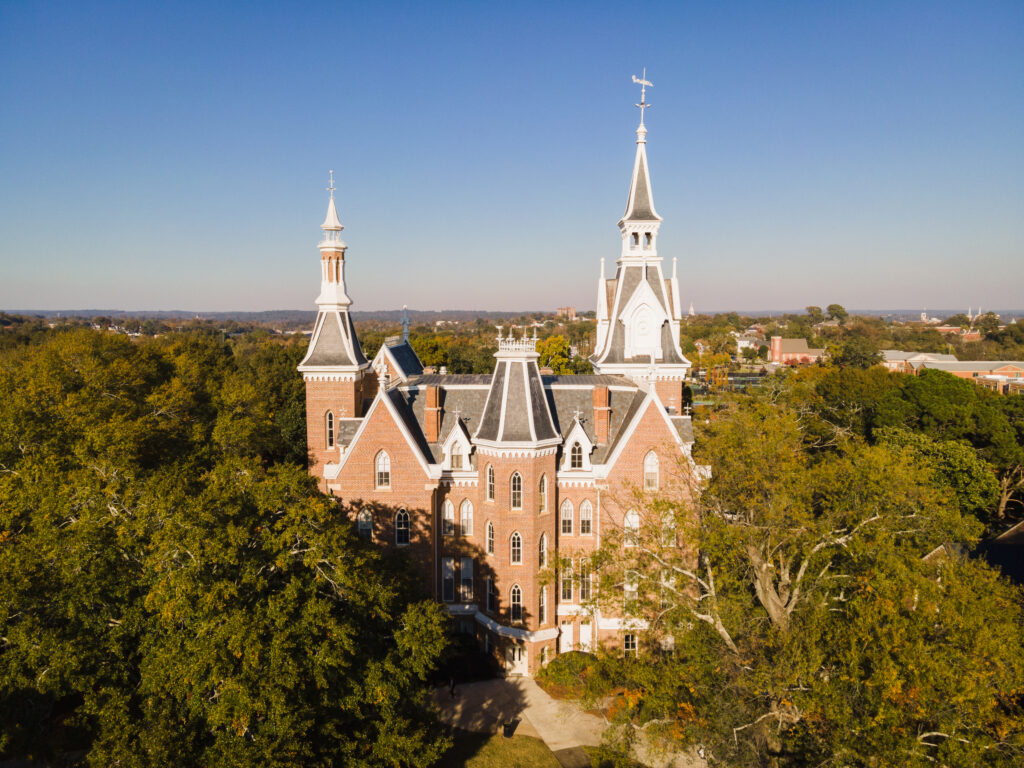 A drone photo of a five-story brick building with tall spires, with trees surrounding it.