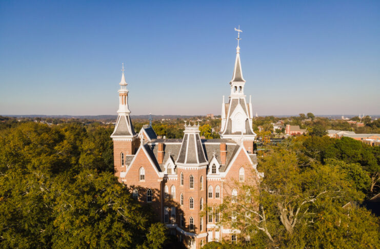 A drone photo of a five-story brick building with tall spires, with trees surrounding it.