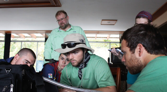Mercer works to reduce mercury pollution in artisanal and small-scale gold mining people in green shirts gather around a laptop