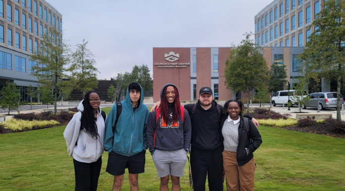 CyBears team advances in competition while teaching students cybersecurity skills Five students stand in a row for a picture outside, in front of a brick building.