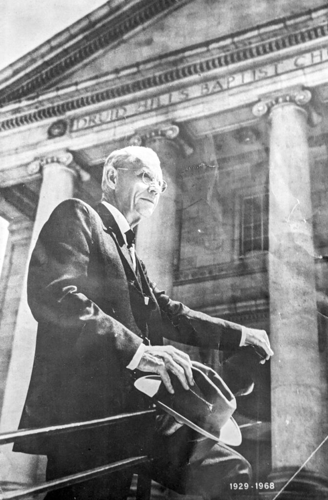 a black and white photo of a man in a suit in front of a building with columns