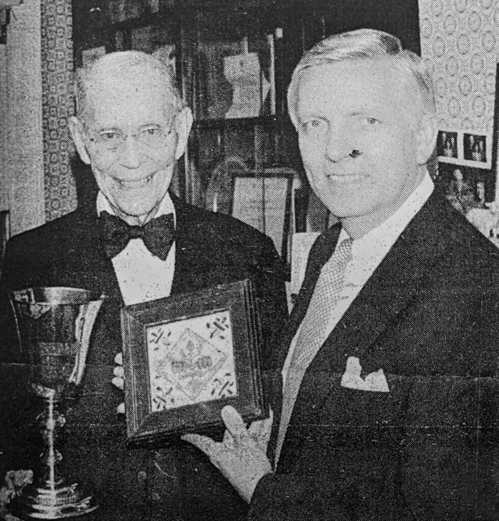 black and white photo of two men. one holds a chalice and one holds a tile