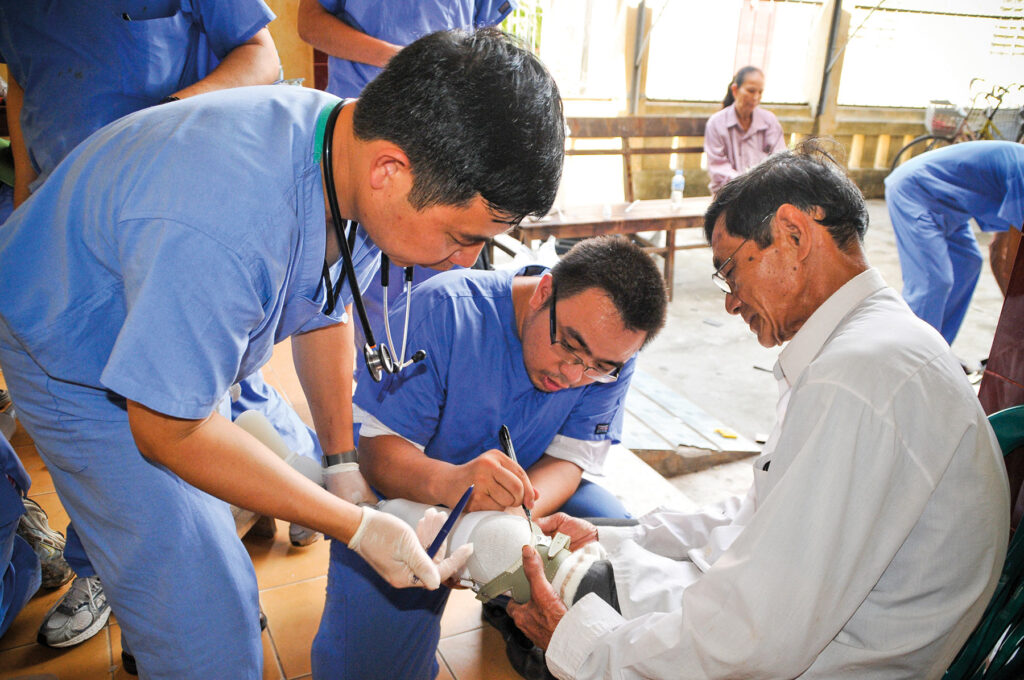 two men in scrubs fit a prosthesis on a man